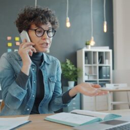 Woman talking on phone at desk with laptop