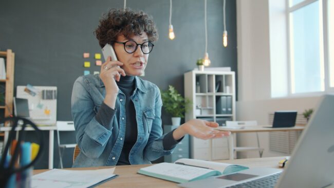 Woman talking on phone at desk with laptop