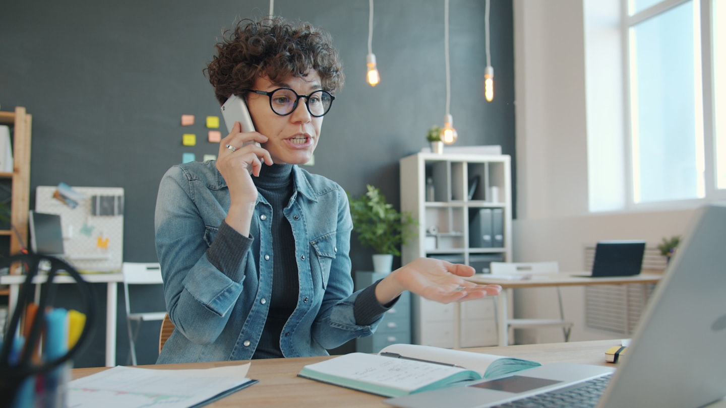 Woman talking on phone at desk with laptop