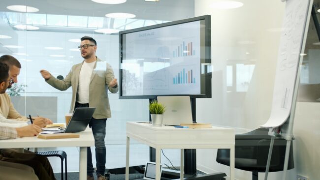 Man presenting data on a large screen to colleagues