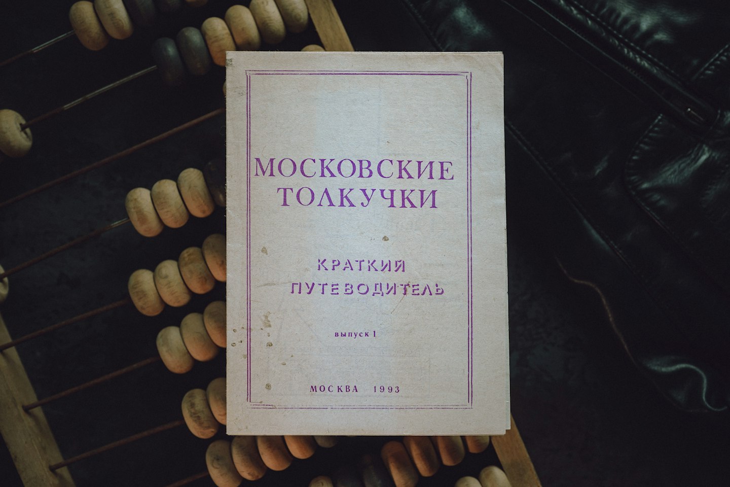A vintage Moscow guidebook — "Moskovskie Tolkuchki" (Brief Guide, 1993) — rests on a worn abacus and dark leather.
