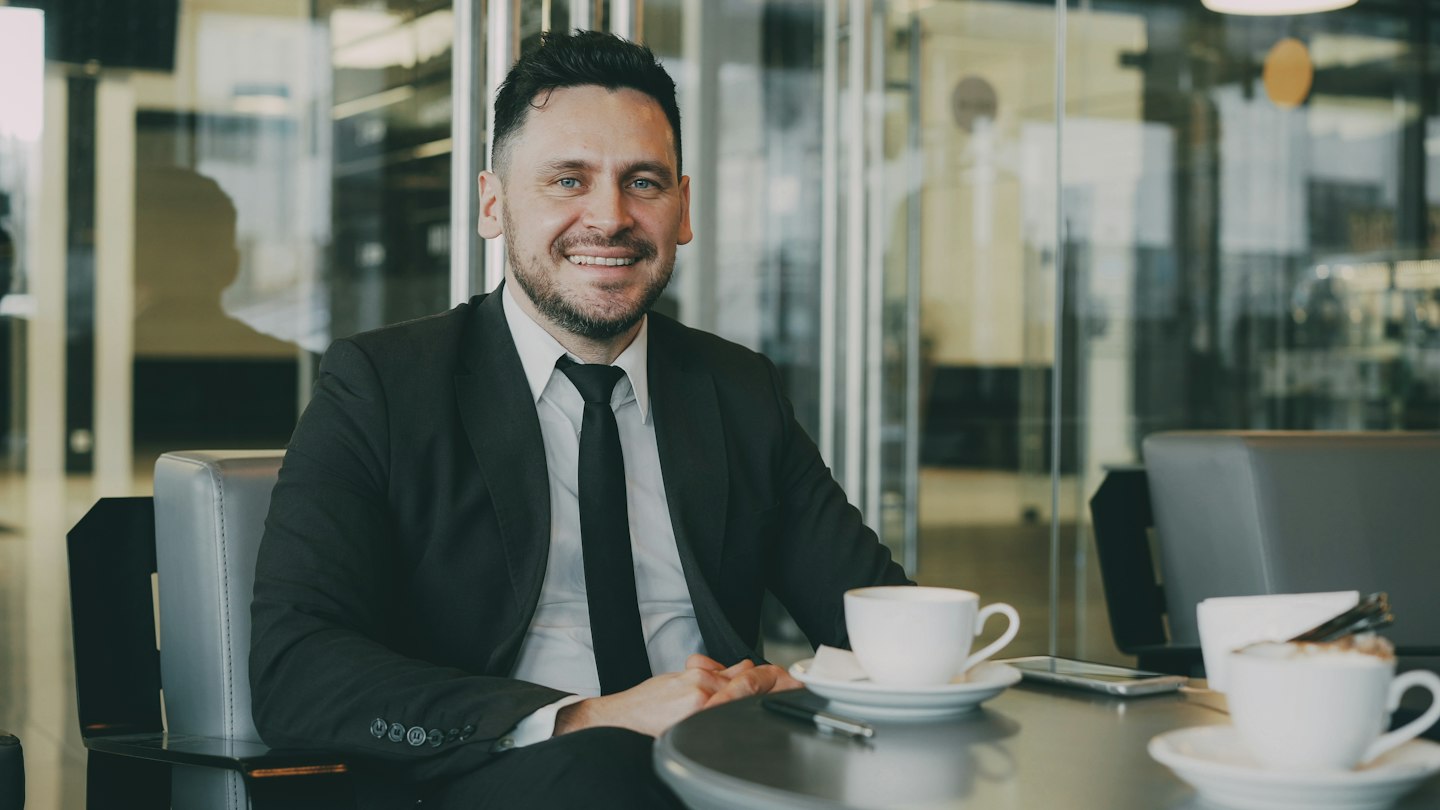 Smiling businessman sitting at cafe table with coffee