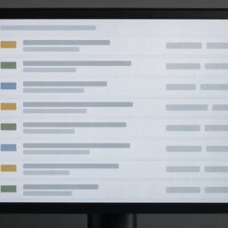 Крупный фронтальный вид монитора с реестром технического долга в виде рядов карточек, нейтральных цветовых меток и полей оценки без читаемого текста.